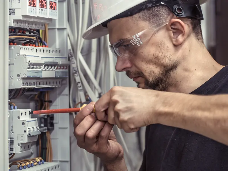 Eletricista conectando cabo em quadro de distribuição com disjuntores
